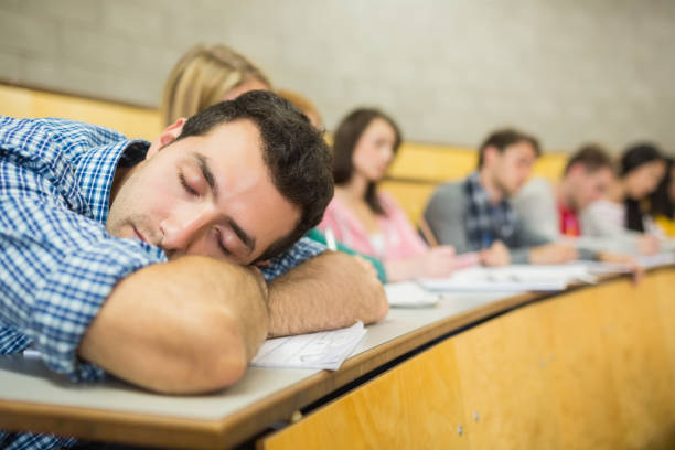 Male sleeping with students in lecture hall Male sleeping with students sitting in the college lecture hall male college student sleeping through lecture stock pictures, royalty-free photos & images