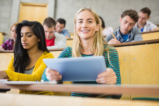 Portrait of a female holding tablet PC with students at the lecture hall