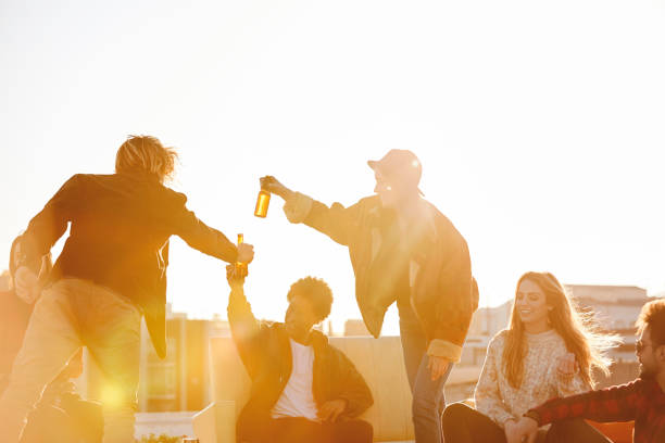 Happy friends enjoying beer on building terrace. Men and women are spending leisure time during summer. They are wearing casuals.