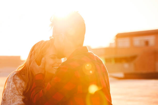 Man kissing on smiling girlfriend's forehead. Young couple spending leisure time on building terrace. They are wearing casuals.