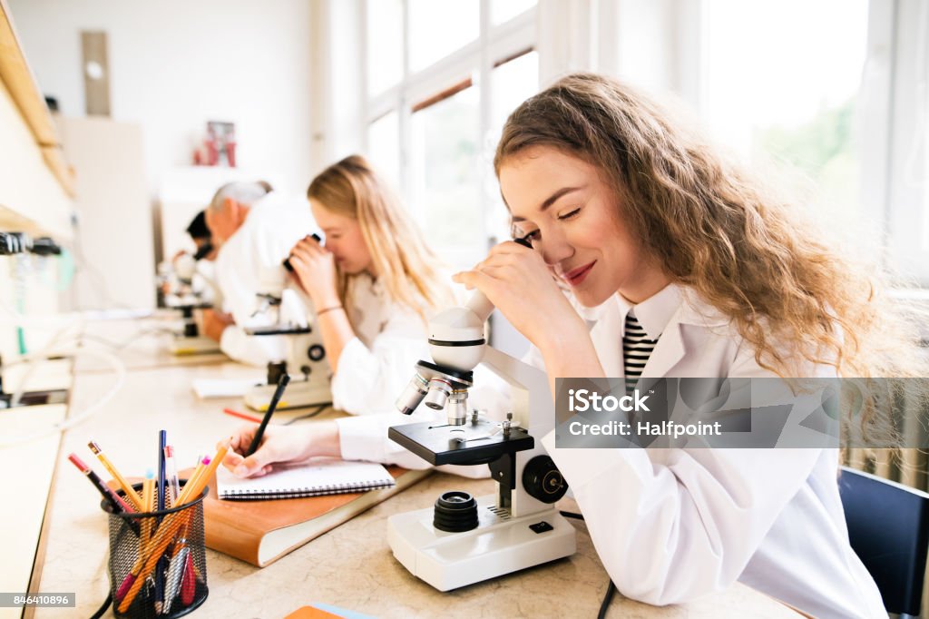 Beautiful high school students with microscopes in laboratory. Beautiful high school students with microscopes in laboratory. Senior teacher teaching biology. Science Stock Photo