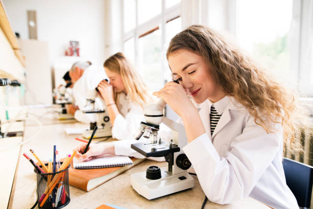 Beautiful high school students with microscopes in laboratory. Beautiful high school students with microscopes in laboratory. Senior teacher teaching biology. high school building stock pictures, royalty-free photos & images