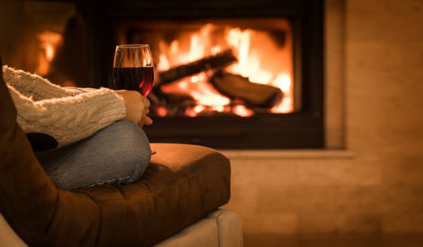 Young woman sitting at home by the fireplace and drinking a red wine. stock photo