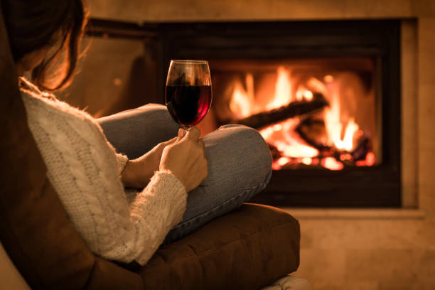 Young woman sitting at home by the fireplace and drinking a red wine. stock photo