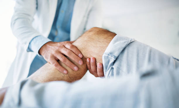 Senior man having medical exam. Closeup side view of early 30's unrecognizable doctor examining a knee of a senior gentleman during an appointment. The doctor is gently touching the tendons around the knee and the knee cap and trying to determine the cause of pain. ache stock pictures, royalty-free photos & images