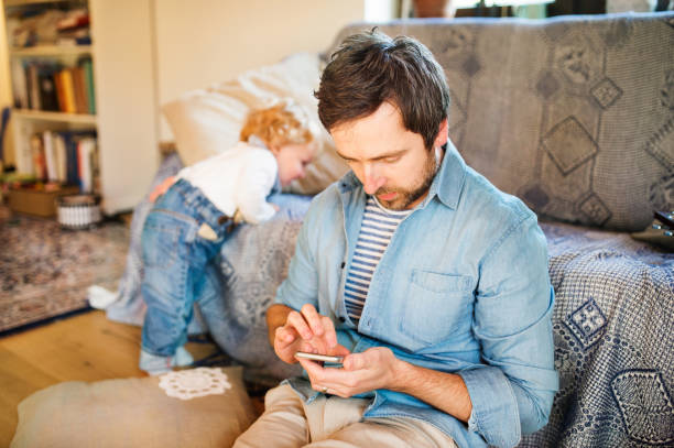 Young father with smartphone at home with his little son.