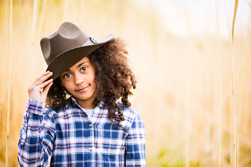 Beautiful african american girl with curly hair in checked shirt and hat outdoors in field.