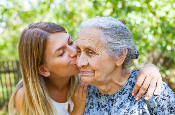 Familiy time - kiss Young woman kissing her old grandmother in the park alzheimer patient stock pictures, royalty-free photos & images