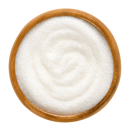 Fine granulated white sugar in wooden bowl. Crystals of refined table sugar. Sweet soluble carbohydrates. Sucrose, disaccharide of glucose and fructose. Macro food photo close up from above over white
