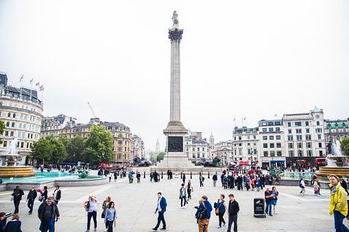 Crowds of people going about taking pictures or making their way through Trafalgar Square.