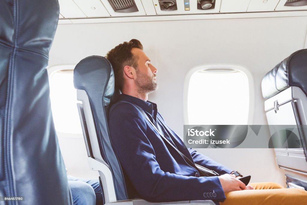 Businessman traveling by flight Side view shot of mature man sitting in airplane seat and looking outside the window. Businessman traveling by flight. Airplane Stock Photo