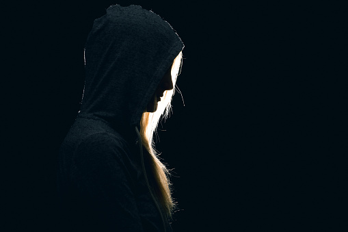 The silhouette of a sad woman wearing a hoodie in a dark place.