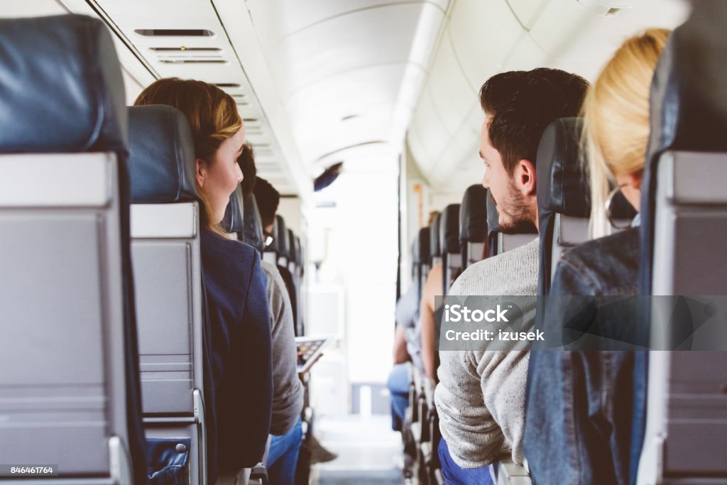 Commercial airliner cabin with people travelling Interior of airplane with people sitting on seats and talking. Rear view of commercial airliner cabin. Adult Stock Photo