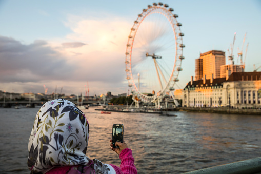 London, United Kingdom - September 9, 2017: The famous tourist attraction London Eye in central London and the City Skyline on the River Thames at dusk shot by a muslim tourist.