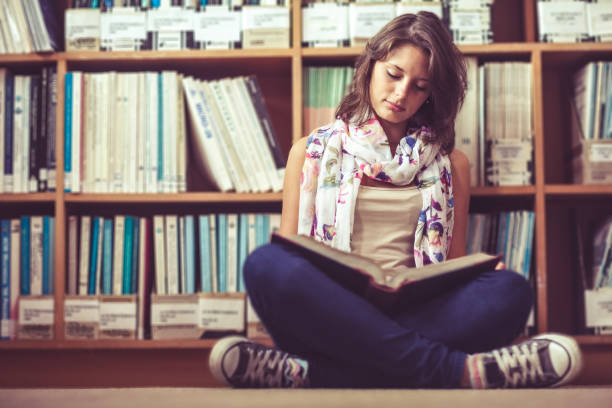 istock Female student against bookshelf reading a book on the library floor 846492030