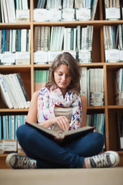 istock Female student against bookshelf reading a book on the library floor 846492072