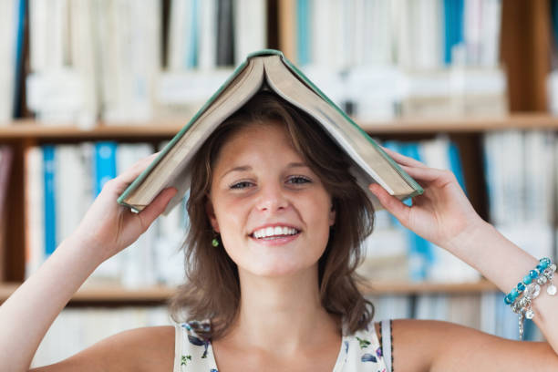 istock Female student holding book over her head in library 846492784