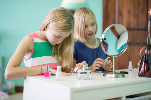 Two young sisters do makeup in bathroom together. They are giving themselves manicures.