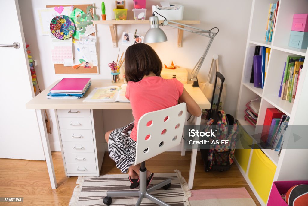 Young girl doing homework School girl doing homework at home in her desk. Back view. Child Stock Photo