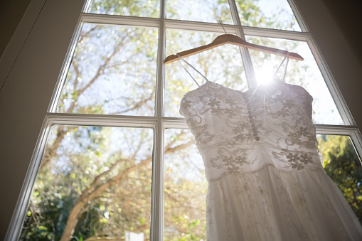 Low angle view of wedding dress hanging on window in fitting room