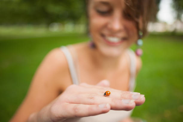 Close up of a smiling blurred young woman gently holding a ladybug at a park