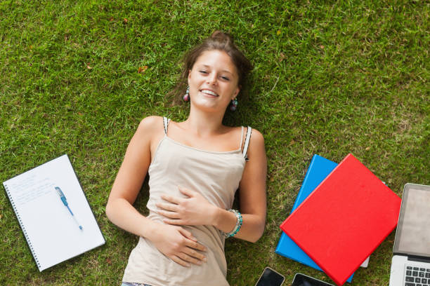 istock Smiling young woman lying on grass with books 846558800