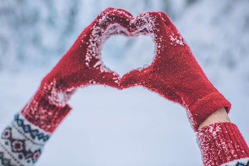 Women make heart shape with hands in winter gloves. Idyllic snowy winter atmosphere.