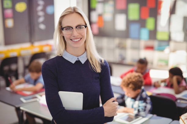 Portrait of happy teacher standing with arms crossed in classroom Portrait of happy teacher standing with arms crossed in classroom at school elementary age stock pictures, royalty-free photos & images
