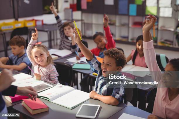 Photo libre de droit de Collégiens Levant Leurs Mains Dans La Salle De Classe banque d'images et plus d'images libres de droit de Enfant