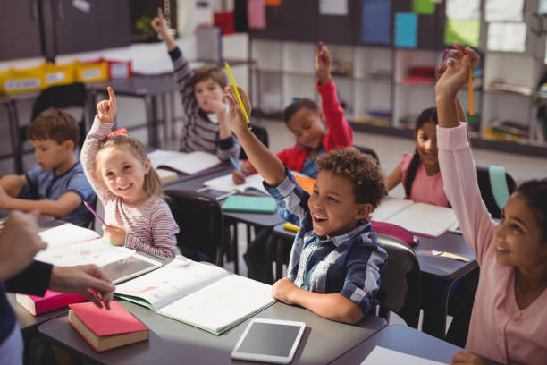 Schoolkids raising their hands in classroom Schoolkids raising their hands in classroom at school primary age child stock pictures, royalty-free photos & images