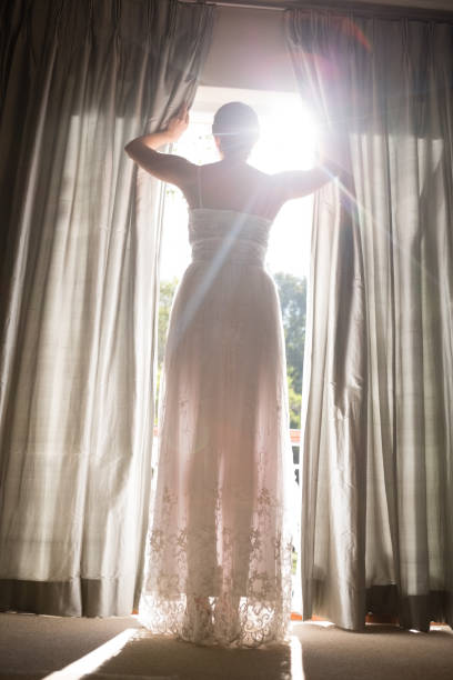 istock Low angle view of bride in wedding dress looking through window at home 846572892