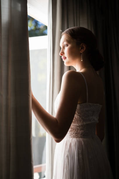 istock Beautiful bride looking through window while standing in darkroom at home 846572898