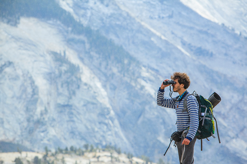 The young man, hipster, tourist - hiker and backpacker, observing the Yosemite from the  Olmsted Point - the overlook near by Tioga Pass. Yosemite National Park, California, USA, North America.