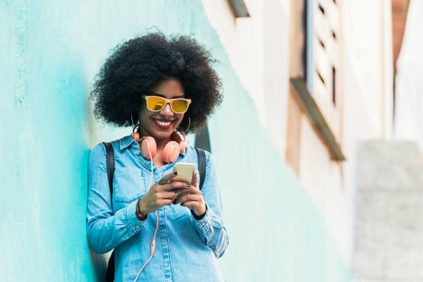 schöne afro amerikanerin mit mobile auf der straße. - junge frau allein stock-fotos und bilder
