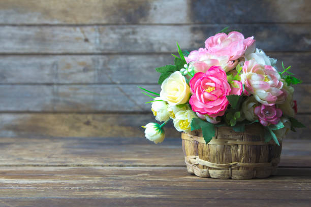 Artificial flowers in rustic wooden vase over colorful artistic grunge wood texture background / interior design element