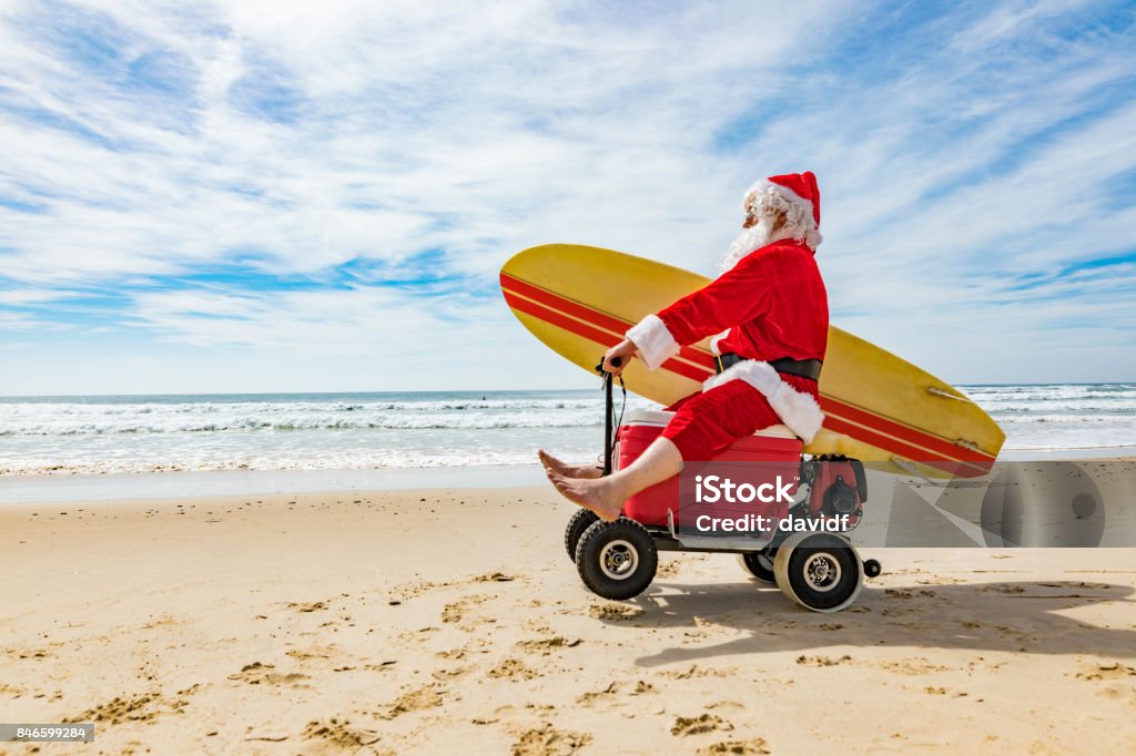 Santa Claus Doing a Wheelie on a Motorised Esky Cooler on the Beach Santa Claus relaxing after Christmas doing a wheelie while riding a motorised esky cooler on the beach Christmas Stock Photo