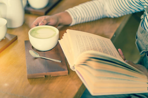 woman reading book while drinking coffee in coffee shop