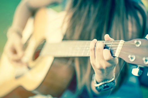 closeup of female's hands playing acoustic guitar with vintage tone