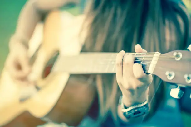 Photo of closeup of female's hands playing acoustic guitar with vintage tone
