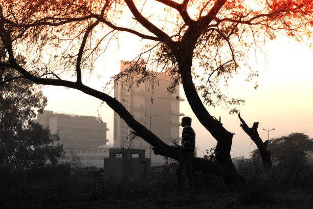 Young man standing near the tree far from the city buildings.
