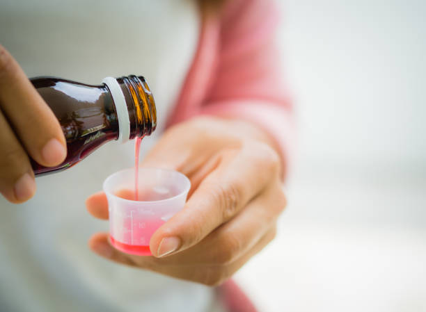 detalle mujer vertiendo jarabe medicamento o antipirético de botella a la copa. - cough remedy fotografías e imágenes de stock