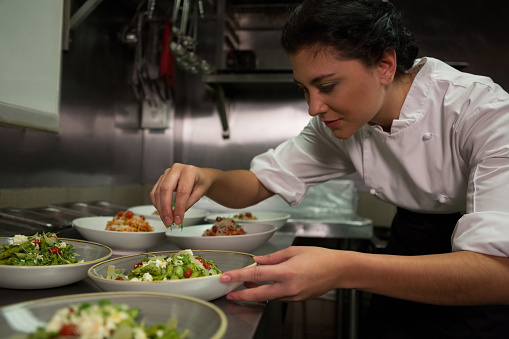 Female chef garnishing appetizer plates at order station in commercial kitchen