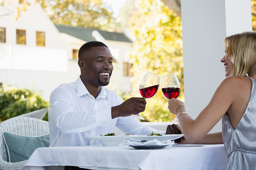 Young couple toasting red wine while sitting at restaurant
