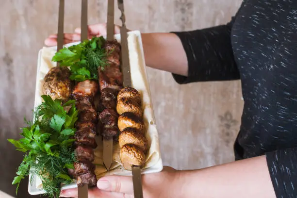 Waiter brings shish-kebab with grilled vegetables on white dish. Meat, field mushrooms and fresh green herbs, barbecue and natural food preparing in restaurant, close up