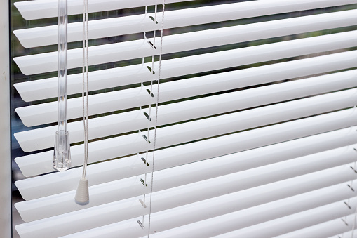Fragment of the white Venetian blinds with lift cord and turning rod of a manual control on a foreground