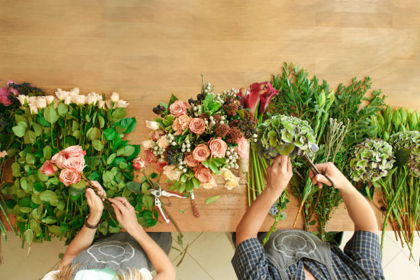 fiorista e assistente nella consegna del negozio di fiori rendono il bouquet di rose, la vista dall'alto del tavolo - composizione di fiori foto e immagini stock