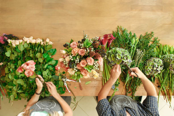 Florist and assistant in flower shop delivery make rose bouquet, table top view