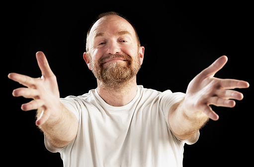 A middle-aged, bearded man smiles widely, holding out his hands in blessing or welcome.