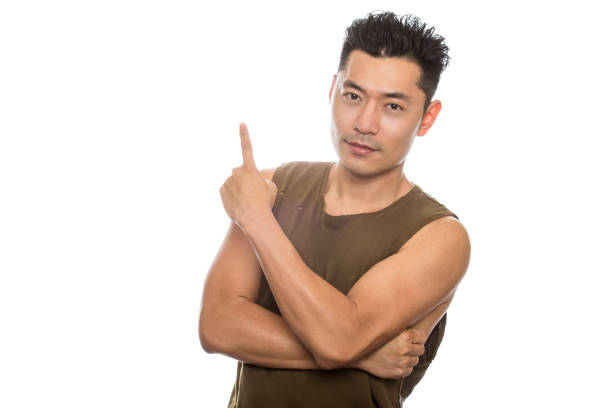 Athletic Asian male with trendy torn sleeveless shirt on a white background.  He is displaying advertising expressions or gestures.  The handsome chinese or japanese man is muscular and physically fit