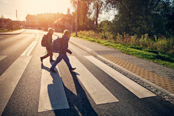 chicos de la escuela caminando por la cebra cruce en el camino a la escuela - crossing fotografías e imágenes de stock